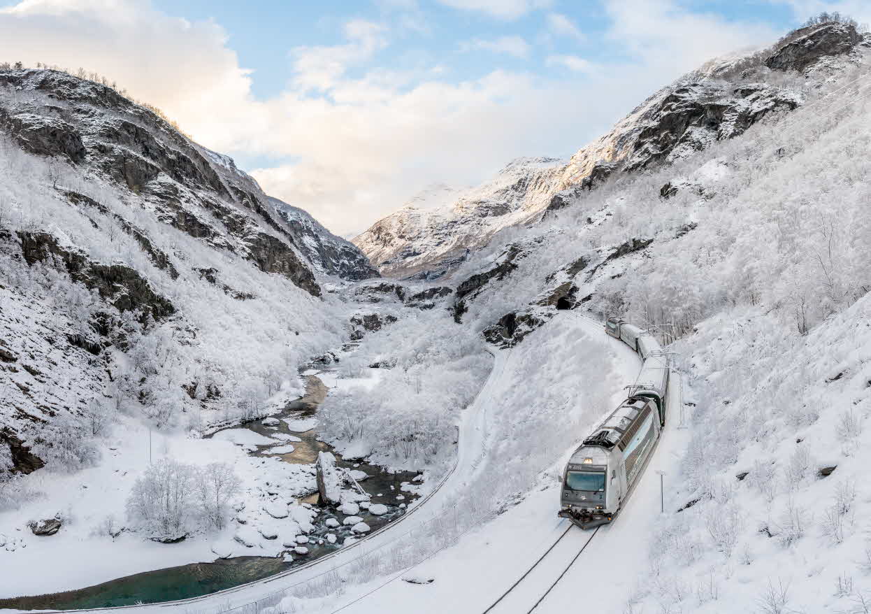 Tog på Flåmsbana kjører langs elva i Flåmsdalen en fin snødag.
