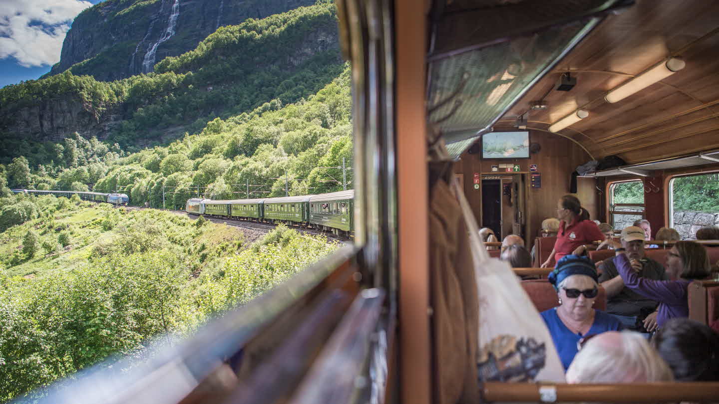 Dos trenes en el ferrocarril de Flåm encontrándose en el valle, vistos desde una ventana del vagón con turistas
