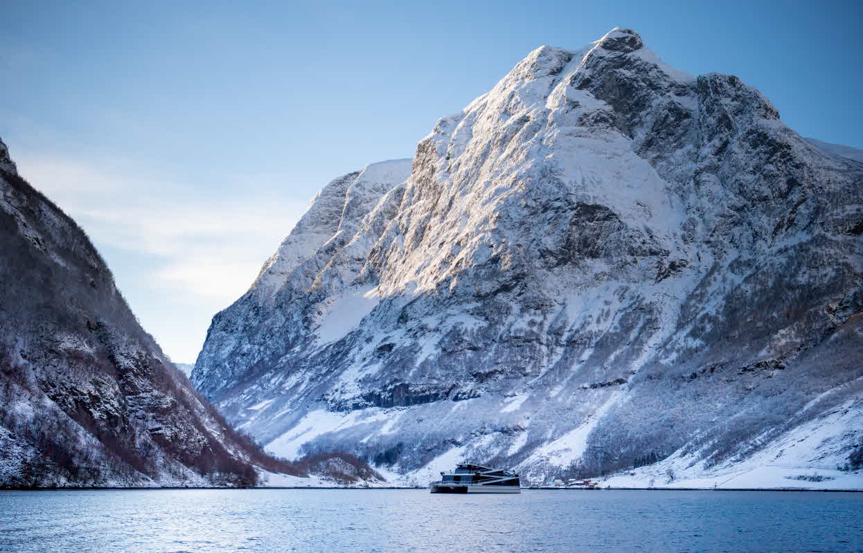 En sightseeingbåt på Nærøyfjorden utenfor Bakka med Bakkanosi over en fin vinterdag