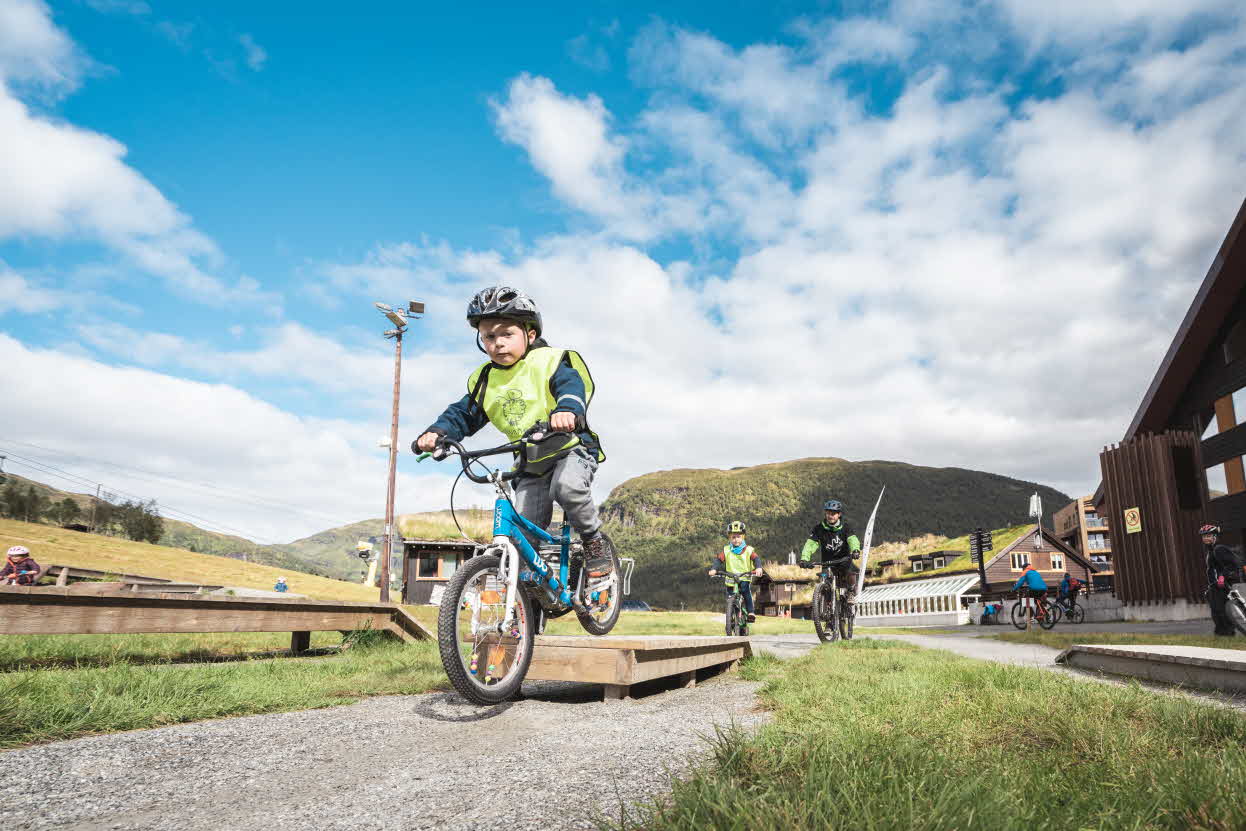 A little boy cycles over an obstacle on the mountain biking trail in Myrkdalen