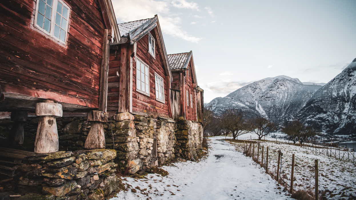 Tre gamle røde hus på Otternes med utsikt mot Flåm en kald vinterdag