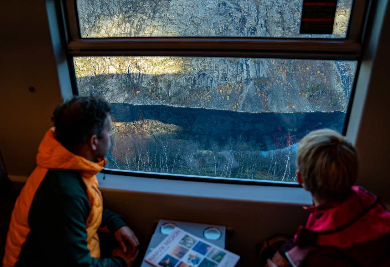 A man and a woman looking down on the Rombak fjord from a window in The Arctic Train