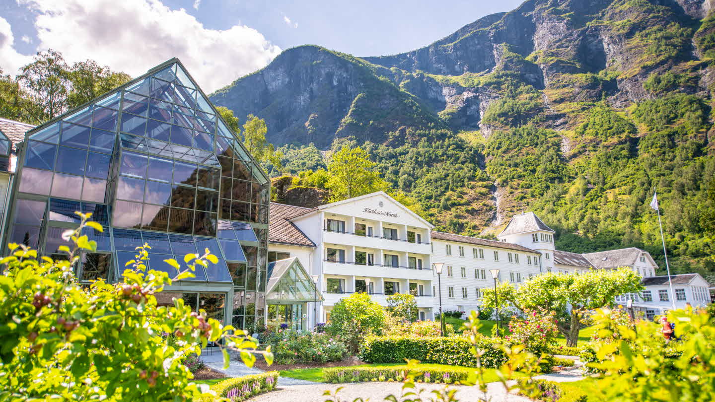 Blomane bognar utanfor Fretheim Hotel i Flåm ein varm sommardag, høge fjell i bakgrunn