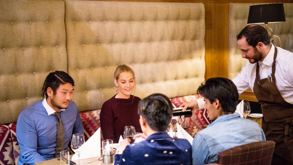 Two couples sitting around a table in restaurant Arven getting red wine served by a waiter