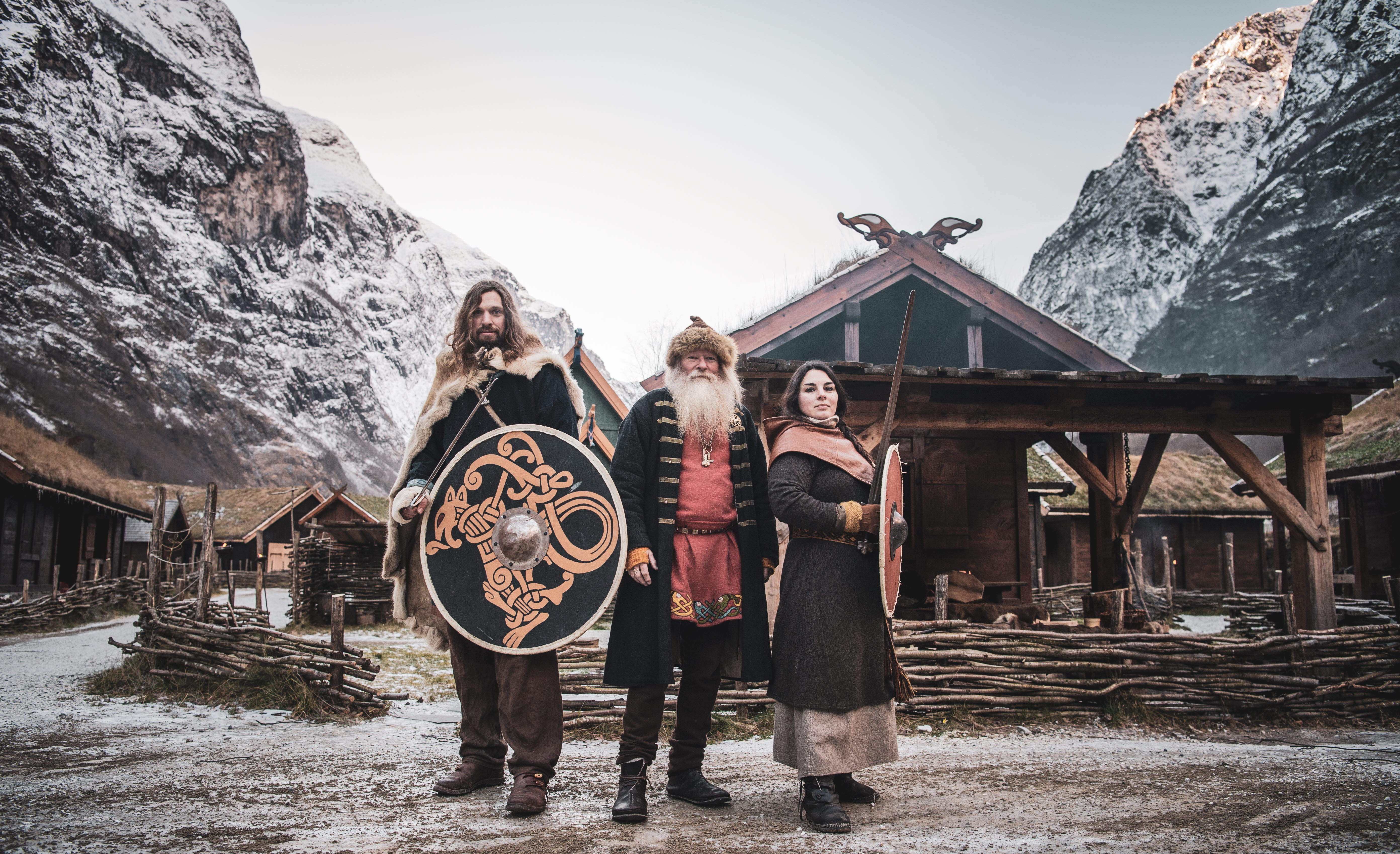 Two male and a female Viking standing in front of Gudvangen Viking villahe with sword and shields.
